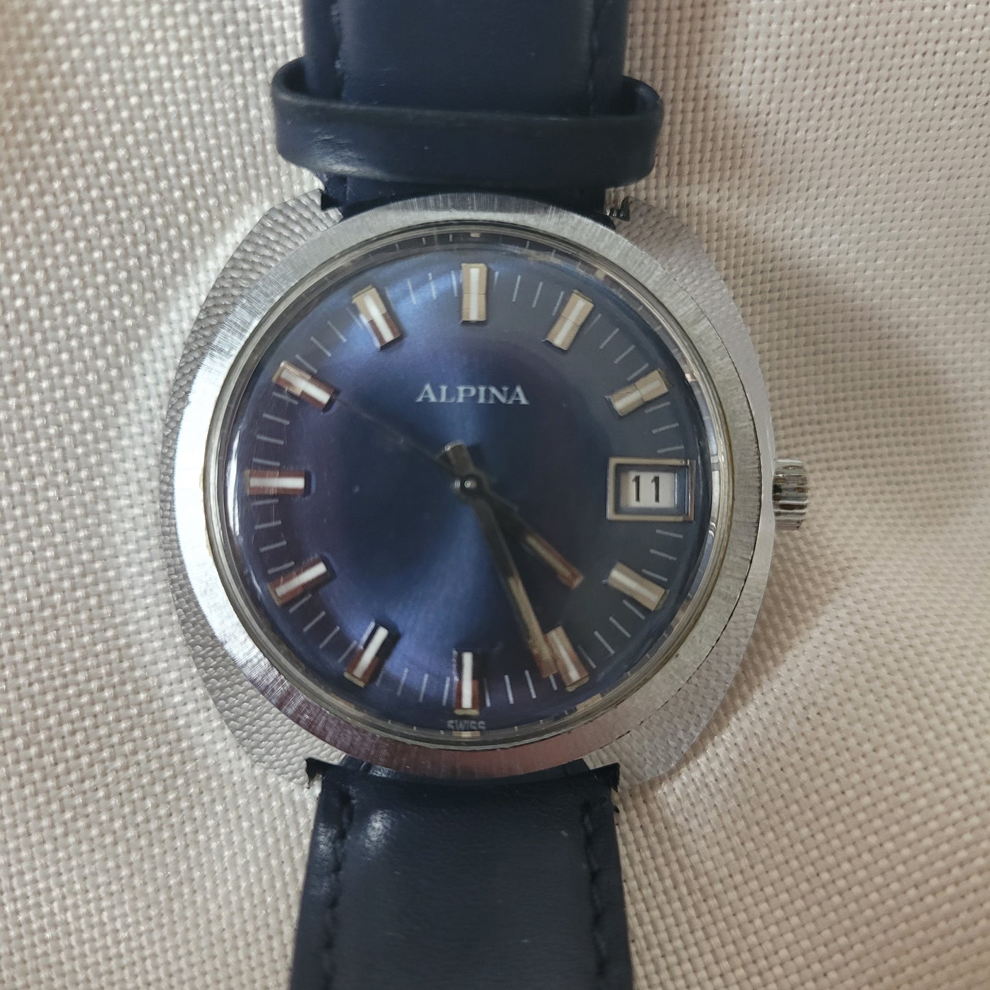 Alpina Vintage Armbanduhr mit blauem Zifferblatt, silbernem Edelstahlgehäuse und Datumsanzeige bei 12 Uhr. Die Uhr besitzt ein dunkelblaues Lederarmband und silberne Indizes mit Leuchtakzenten – klassische Schweizer Vintage-Uhr für Sammler.