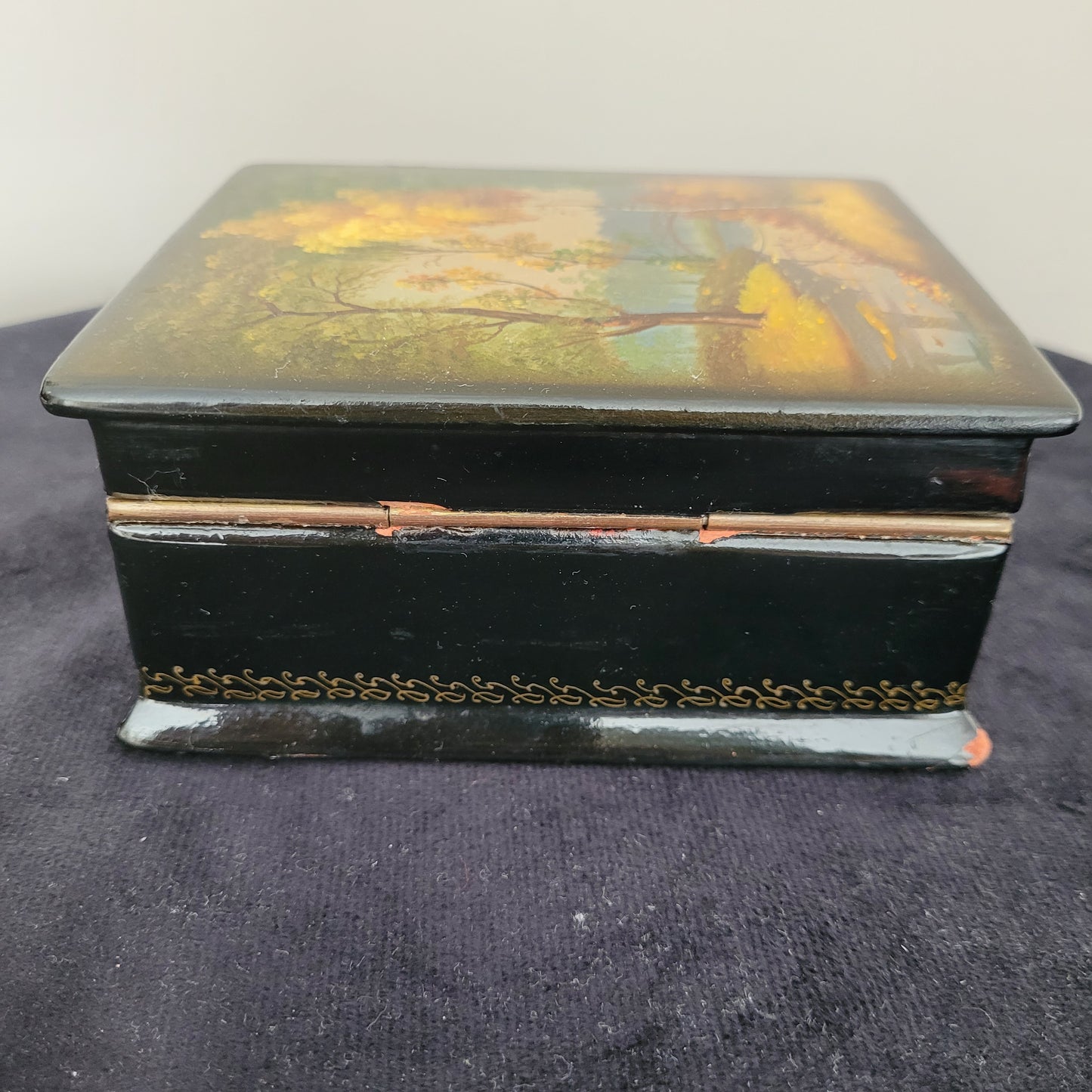 Antike/Vintage Lackdose aus Holz aus der UdSSR – Rückseite mit kunstvollem Landschaftsmotiv Das Bild zeigt die Rückseite einer antiken/Vintage Lackdose aus Holz aus der UdSSR, verziert mit einer detaillierten und farbenfrohen Landschaftsmalerei. Die Szene umfasst einen idyllischen Park mit einem kleinen Teich und einer eleganten Brücke im Hintergrund. Die herbstlichen Farben der Bäume – leuchtendes Gelb, warmes Rot und sattes Grün – verleihen dem Motiv eine nostalgische Atmosphäre.