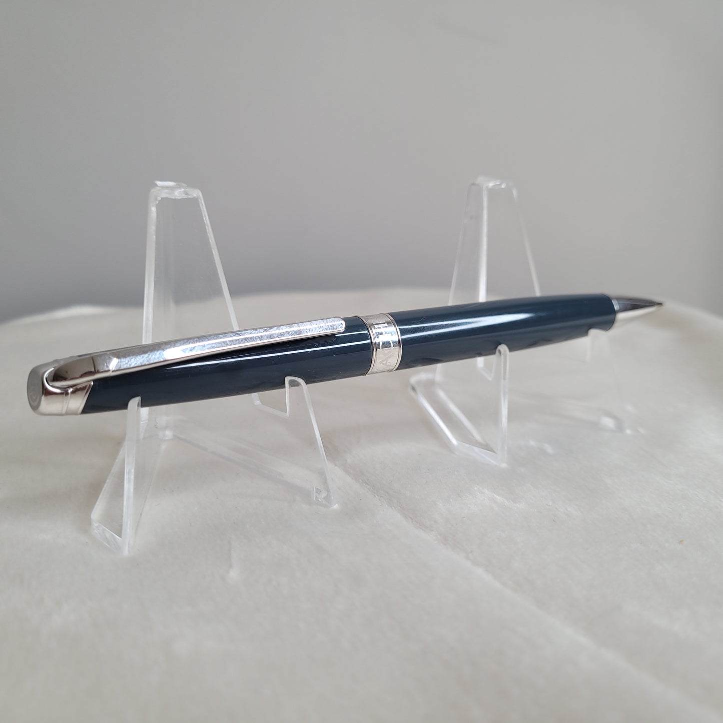 Ein eleganter Caran d'Ache Druckbleistift Leman in Grau-Blau, präsentiert auf einem transparenten Ständer. Der Druckbleistift zeichnet sich durch stilvolles Design und silberne Akzente aus, was die schweizerische Präzision und exzellente Handwerkskunst betont. Ideal als luxuriöses Geschenk oder exklusives Accessoire für das Büro. Swiss Made.