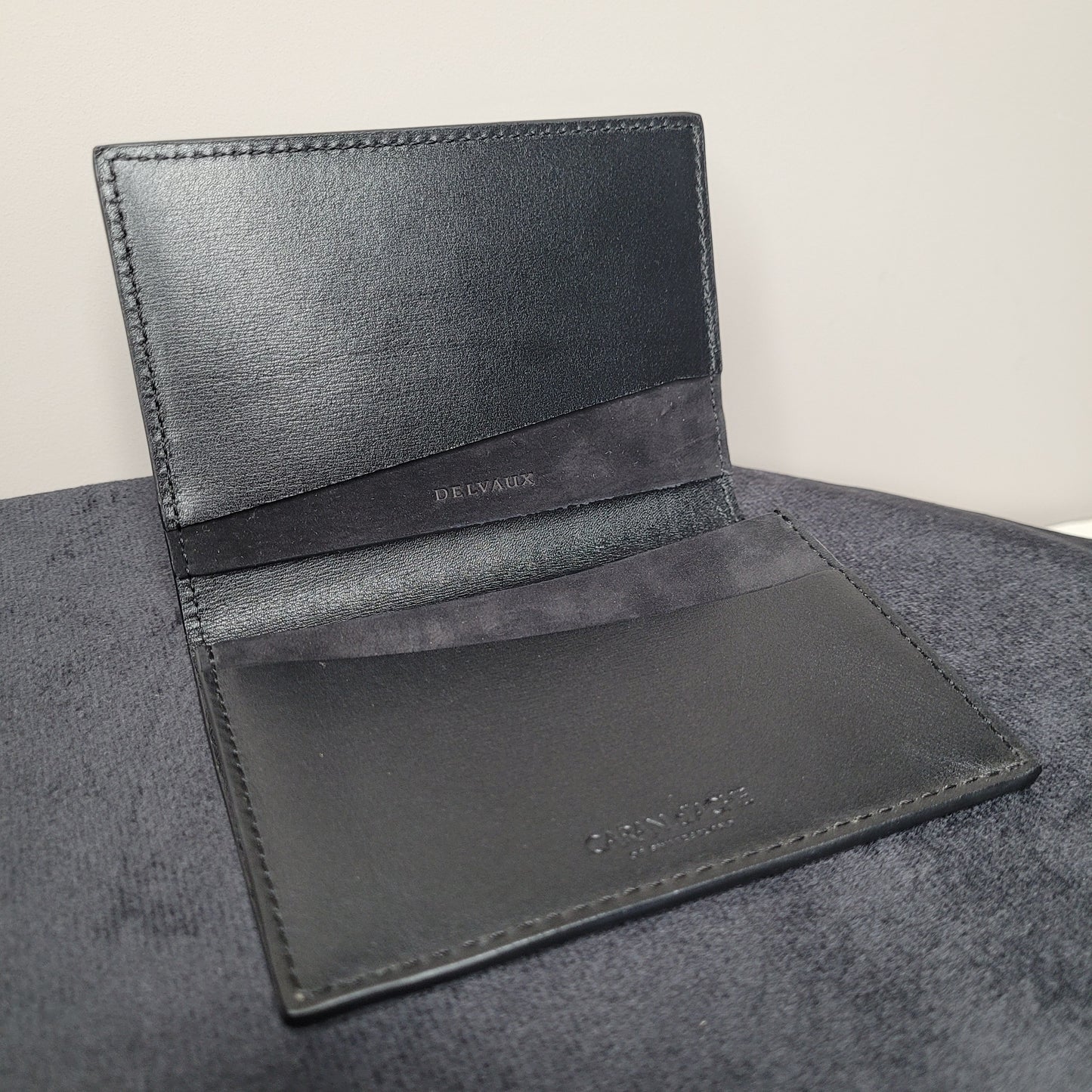 Geöffnetes schwarzes Leder-Visitenkartenetui von Caran d'Ache, entworfen in Zusammenarbeit mit Delvaux, auf schwarzer Stoffoberfläche liegend.