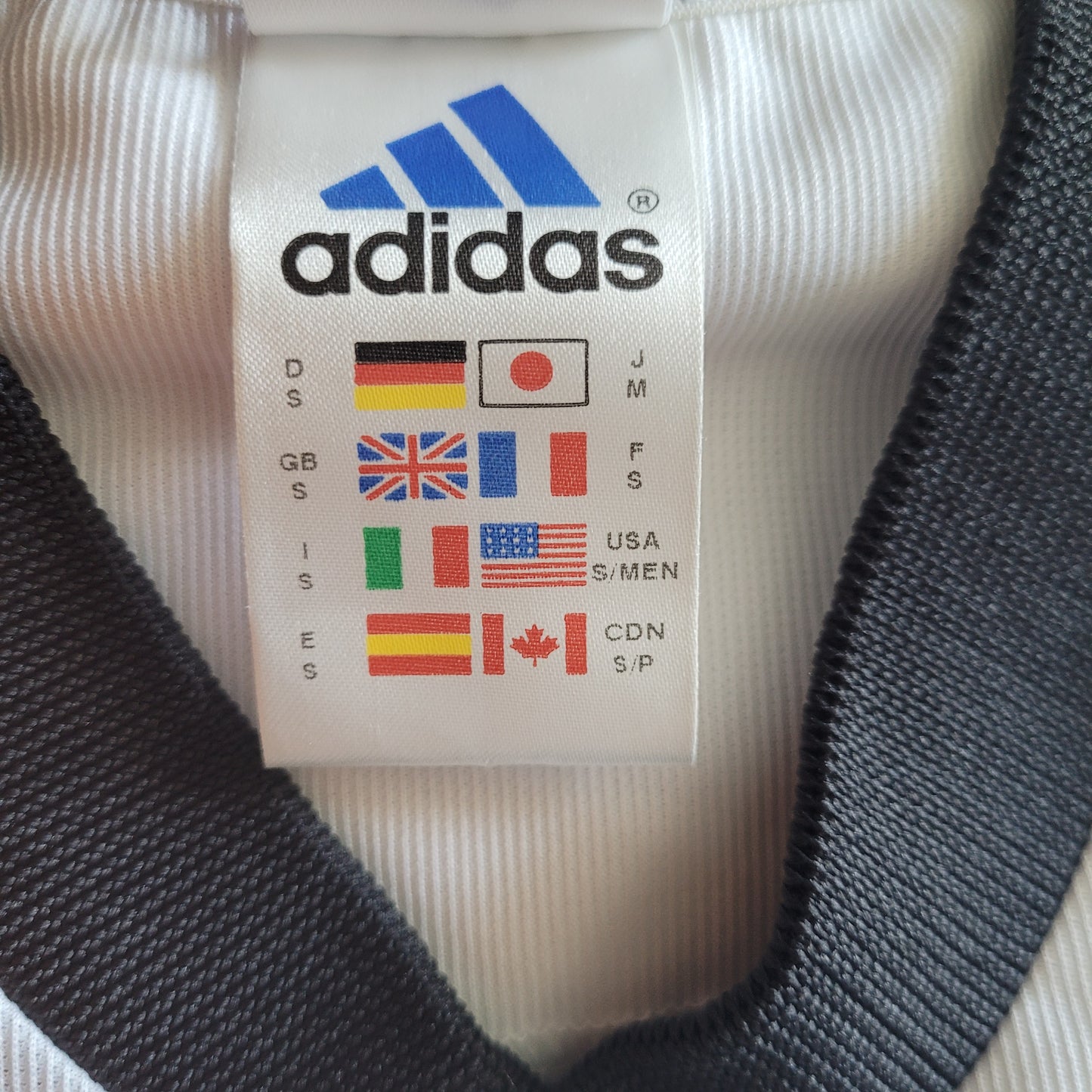 Deutschland DFB Vintage Trikot 2002 - Größe S - Es ist Das Logo von Adidas und verschieden Flaggen mit Kleidungsgrößen zu sehen.