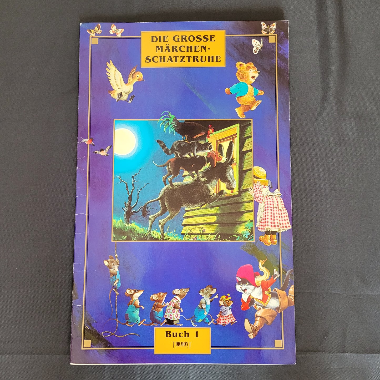 Vintage Cover des Kinderbuchs „Die große Märchenschatztruhe – Buch I“ mit liebevoll gestalteten Illustrationen klassischer Märchenfiguren wie der Wolf und die sieben Geißlein, Bären mit Honigtopf und Mäusen in Kleidung auf dunkelblauem Hintergrund. Das nostalgische Design macht dieses Vintage-Märchenbuch zu einem charmanten Sammlerstück für Liebhaber traditioneller Kinderliteratur und Märchenklassiker.