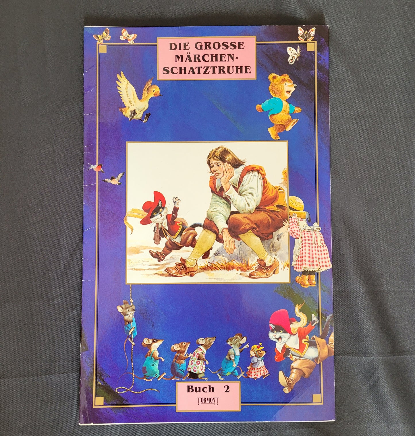 Vintage Cover des Märchenbuchs „Die große Märchenschatztruhe – Buch 2“ mit farbenfrohen Illustrationen klassischer Märchenfiguren wie Zwerge, Tiere in Kleidung und fantasievollen Szenen auf tiefblauem Hintergrund. Das nostalgische Design und die liebevolle Gestaltung machen dieses Vintage-Märchenbuch zu einem begehrten Sammlerstück für Märchenfreunde und Liebhaber traditioneller Kinderliteratur.