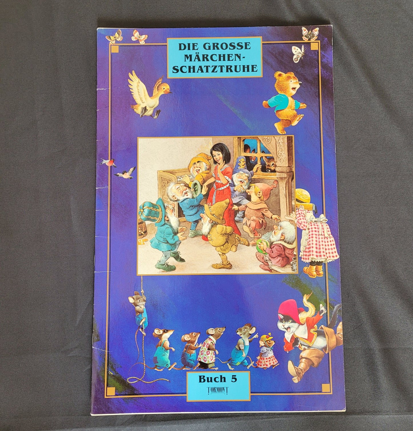 intage Cover des Märchenbuchs „Die große Märchenschatztruhe – Buch 5“ mit farbenfroher Illustration von Schneewittchen und den sieben Zwergen auf violettem Hintergrund, umrahmt von weiteren märchenhaften Figuren wie fliegenden Gänsen und Zwergen. Dieses nostalgische Vintage-Märchenbuch begeistert Sammler und Liebhaber klassischer Kinderliteratur mit seinem liebevoll gestalteten Design und ikonischen Märchenmotiven.