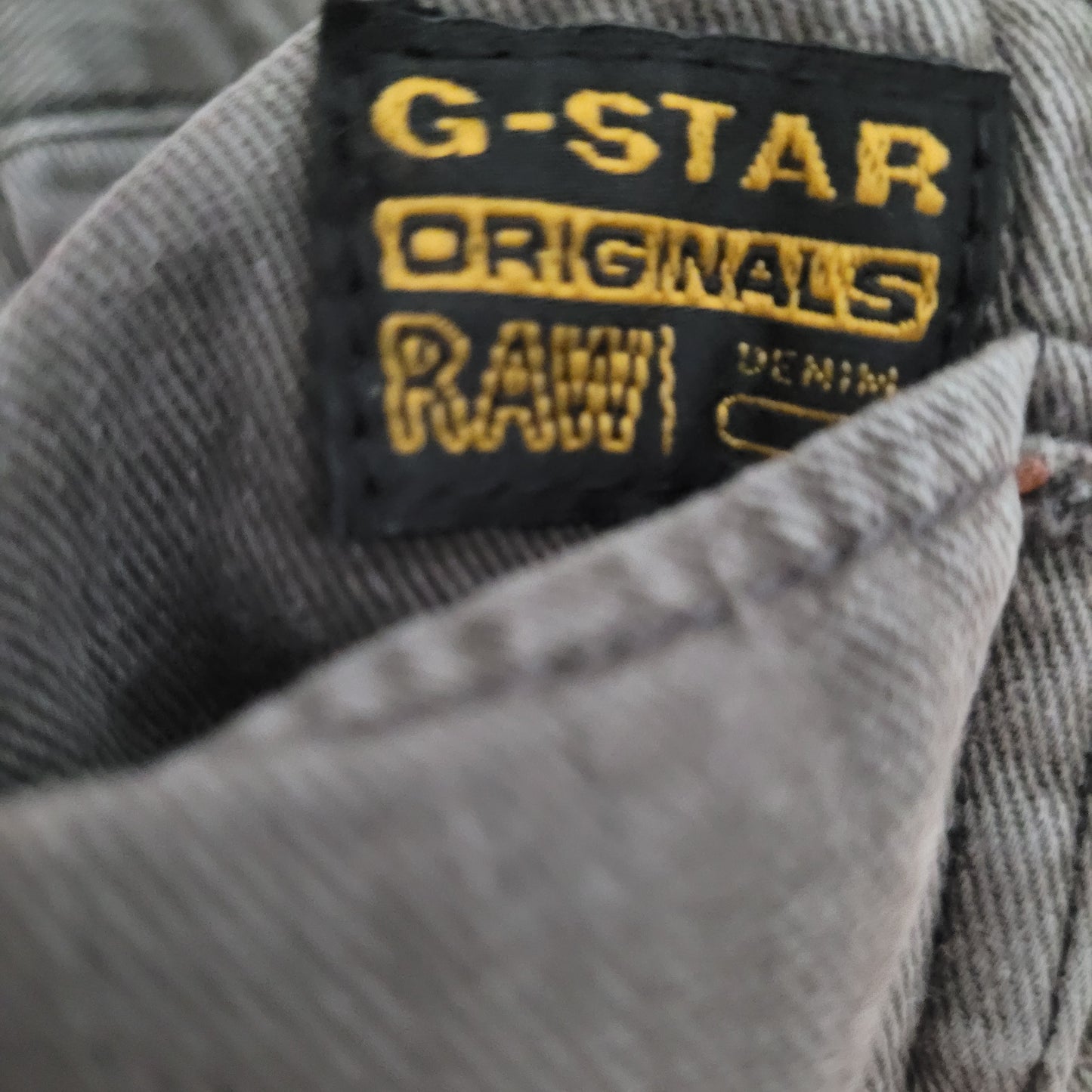 Markenbezeichnung "GStar Raw Originals Denim" auf schwarzem Hintergrund und goldener Schrift zu sehen