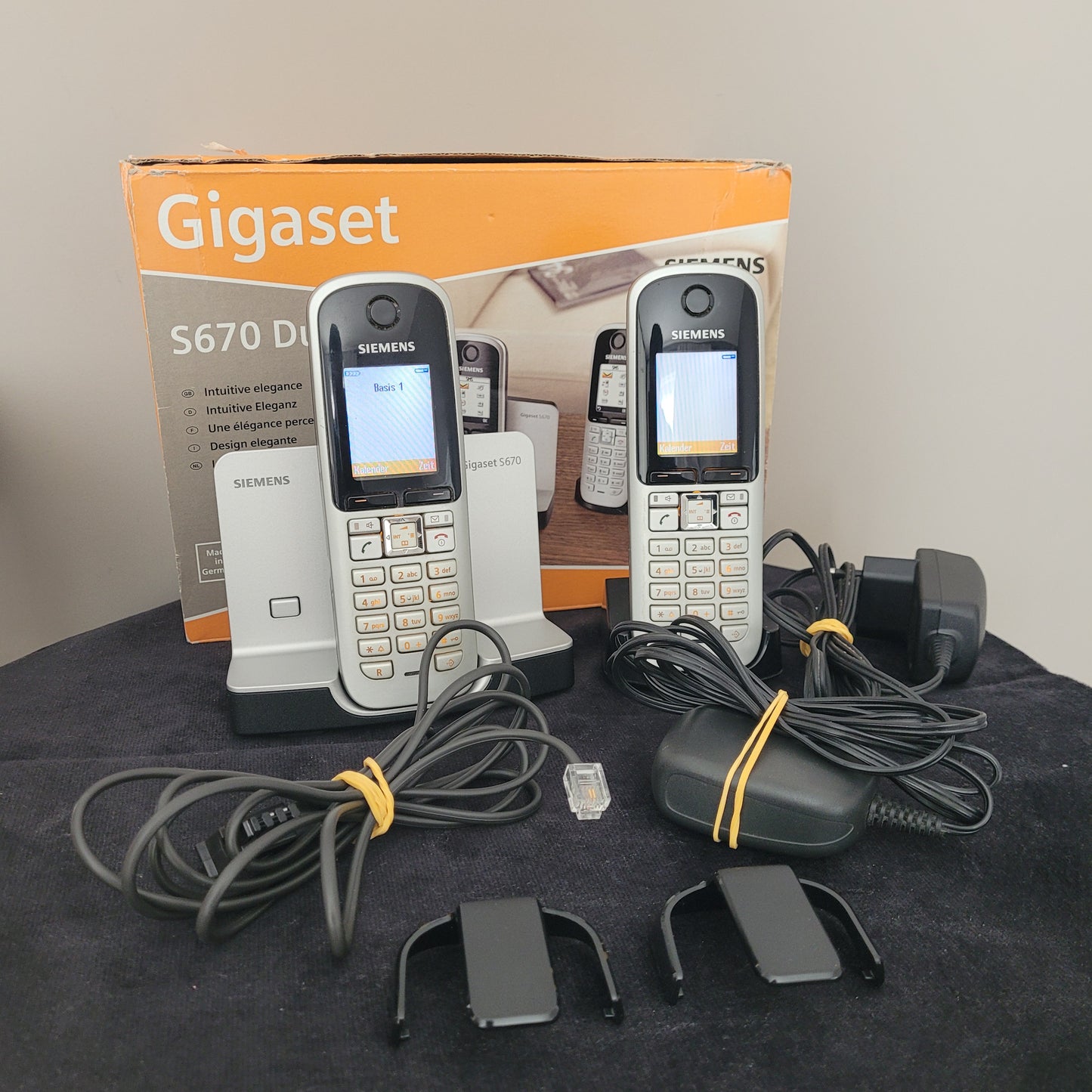 as Gigaset Siemens S670 Duo Eco Dect Titanium Intuitive Eleganz Schnurlostelefon liegt auf einem dunklen Hintergrund. Die beiden Mobilteile sind nebeneinander positioniert und zeigen ihr elegantes Titanium-Finish sowie das intuitive LCD-Display. Das Haupttelefon ist aktiviert, und die Bedienelemente sind klar sichtbar. Ein zuverlässiges DECT-Telefon mit moderner Technologie und stilvollem Design – perfekt für eine hochwertige Kommunikation!