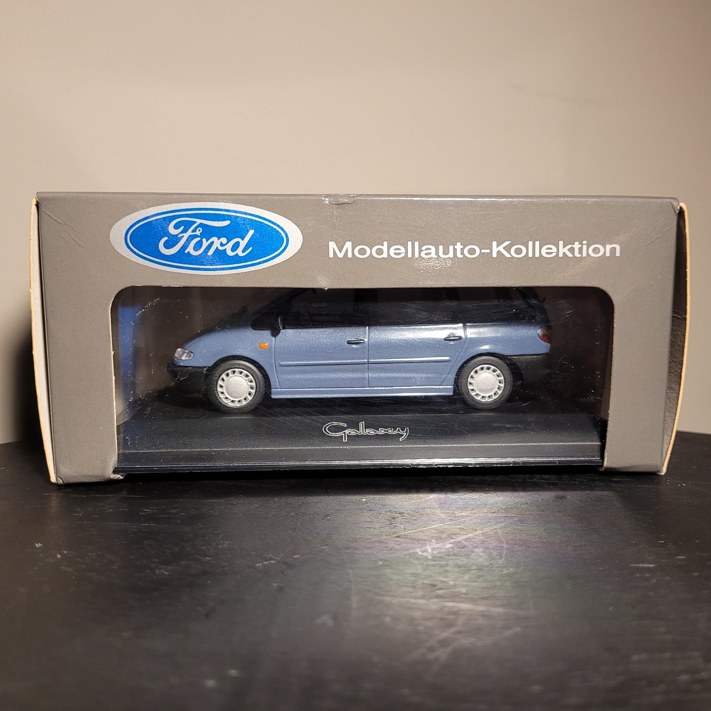 Ein blaues Ford Galaxy Modellauto in einer Verpackung mit der Aufschrift "Modellauto-Kollektion" und einem Ford-Logo oben links. Durch das Sichtfenster der Verpackung ist das Auto gut sichtbar.