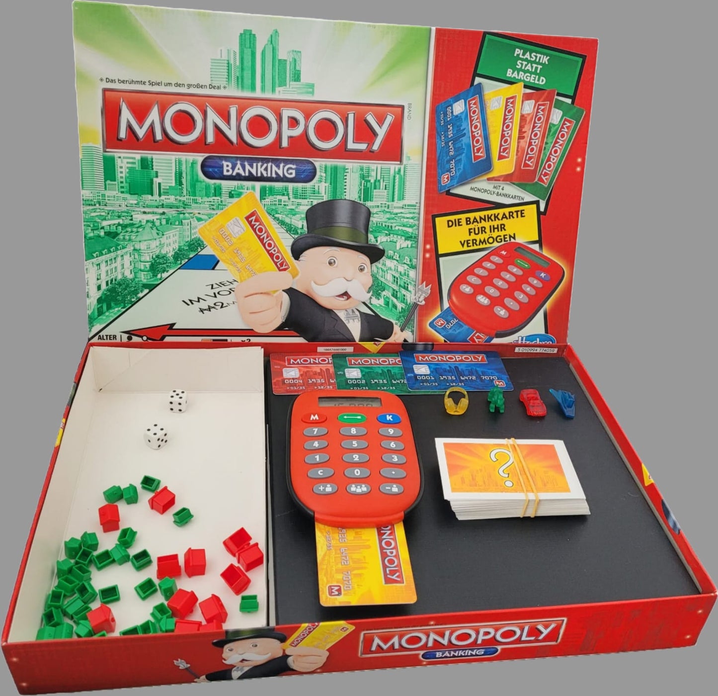Das Bild zeigt die Vorderseite des Monopoly Banking Gesellschaftsspiels von Hasbro. Das Spielbrett ist auf einer dunklen Oberfläche platziert und präsentiert die klassischen Monopoly-Elemente, ergänzt durch moderne Banking-Technologie. Die Spielkarten, Figuren und das elektronische Banking-Gerät sind deutlich sichtbar, was die Vollständigkeit des Sets unterstreicht.