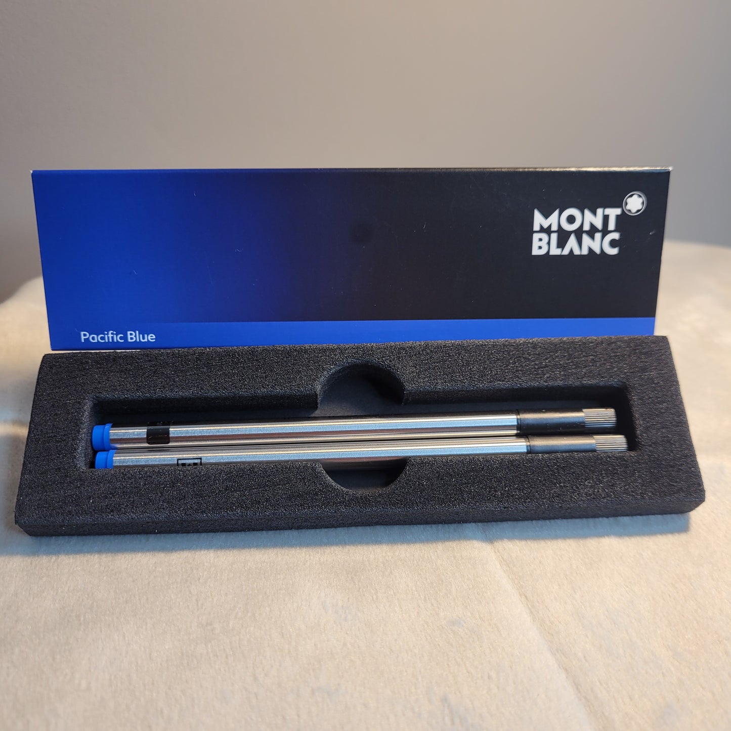 Montblanc-Verpackung mit zwei silbernen Rollerballminen in Pacific Blue, verpackt in schwarzer Schaumstoffhalterung. Elegantes Schwarz-Blau-Design mit Montblanc-Logo und Aufschrift 'Pacific Blue'.