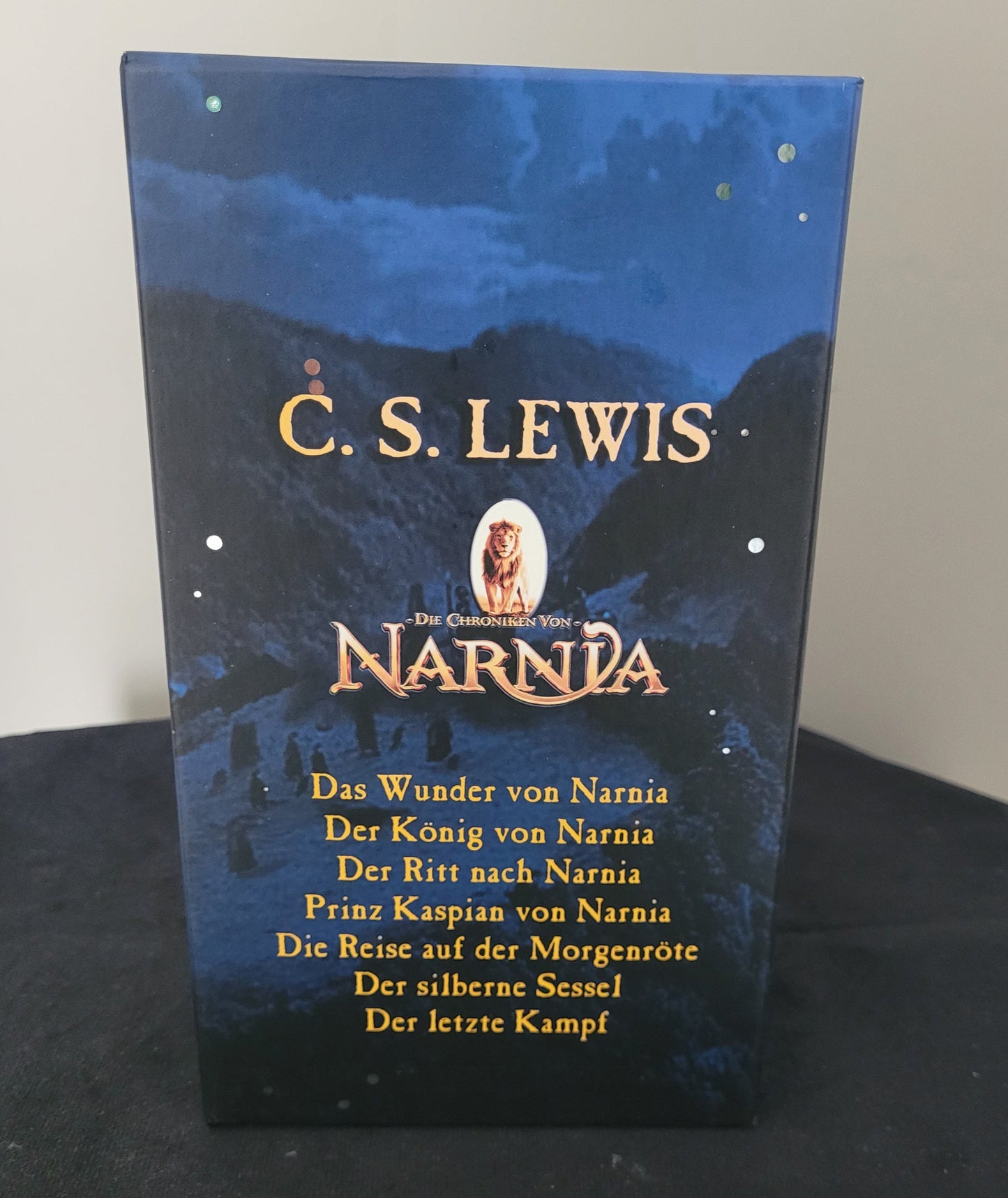 Das Bild zeigt die Rückseite des Buchsets „Die Chroniken von Narnia“ von C.S. Lewis. Sichtbar sind die Buchrücken aller sieben Bände, die nebeneinander aufgereiht sind und eine harmonische Einheit bilden. Die Titel der einzelnen Bücher sind klar lesbar, sodass die Vollständigkeit des Sets ersichtlich wird. Das Set ist auf einem dunklen Untergrund platziert, was die Farben und Details der Buchrücken besonders hervorhebt.