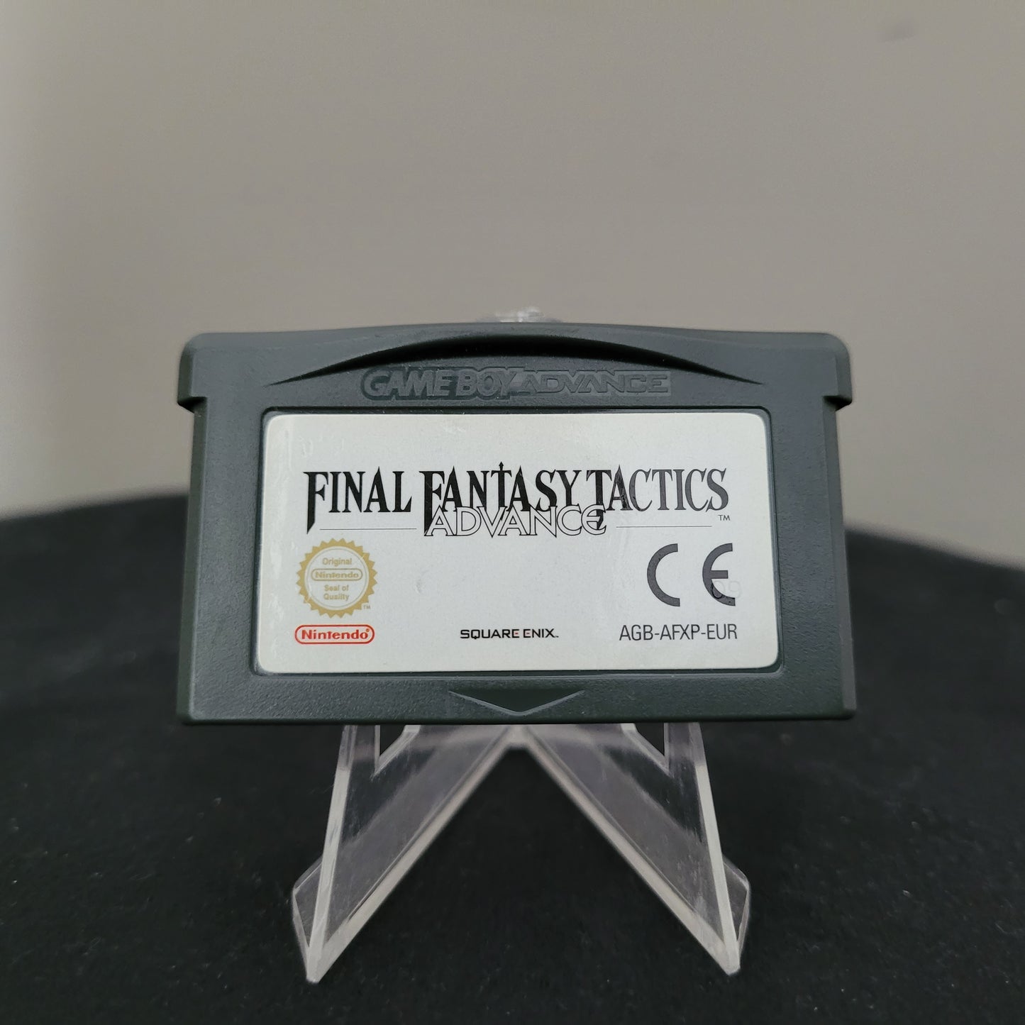 Original Nintendo Game Boy Advance Spiel Final Fantasy Tactics Advance, Modellnummer AGB-AFXP-EUR, auf einem transparenten Ständer präsentiert. Das Spielmodul zeigt das Nintendo-Logo, das Square Enix-Logo und die CE-Kennzeichnung. Dieses geprüfte und voll funktionsfähige Nintendo-Spiel ist ein Klassiker für Retro-Fans und Sammler.