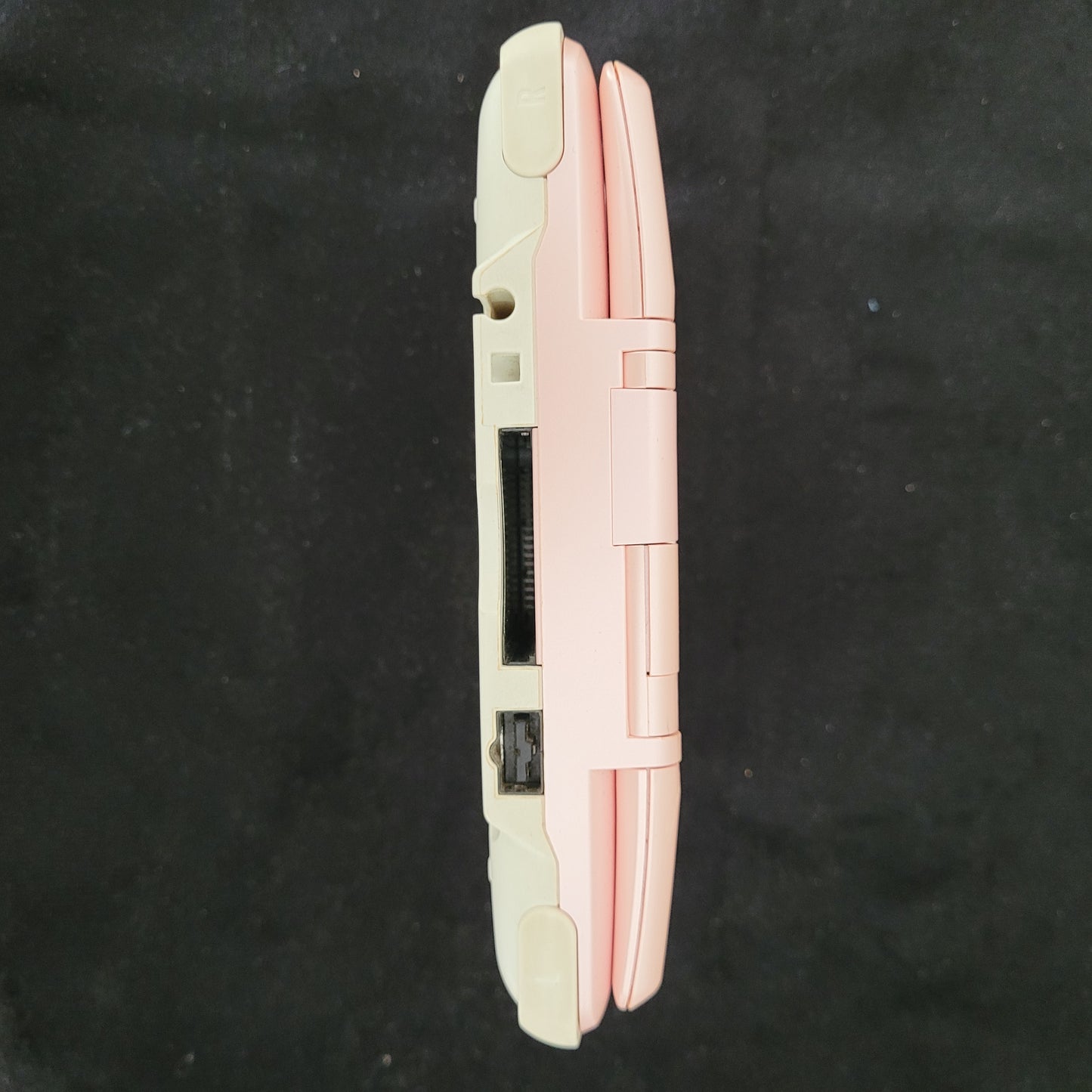 Seitenansicht der Nintendo DS Pink Model No NTR-001 Handheld Konsole, liegend auf schwarzem Untergrund.