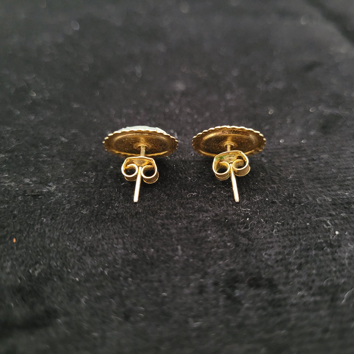Rückseite von zwei goldenen Ohrringen auf schwarzem Hintergrund. Die Ohrringe haben eine runde Form mit gezacktem Rand und dekorativen Verschlüssen.