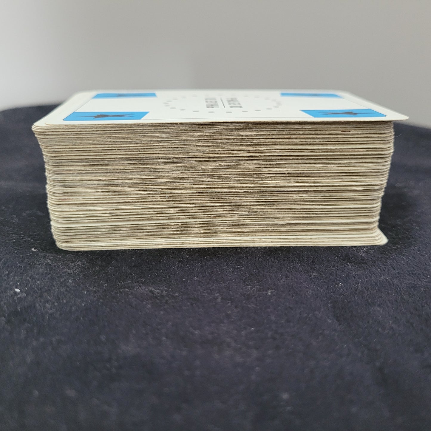 Seitenansicht eines Stapels Phase 10 FX 1998 Ravensburger Vintage Version Spielkarten. Die Karten zeigen Gebrauchsspuren und sind leicht abgenutzt, was ihren Retro-Charme unterstreicht. Auf der Oberseite sind blaue und weiße Markierungen sichtbar. Dieses Vintage-Gesellschaftsspiel ist ein Klassiker für Sammler und Fans von Ravensburger Gesellschaftsspielen.