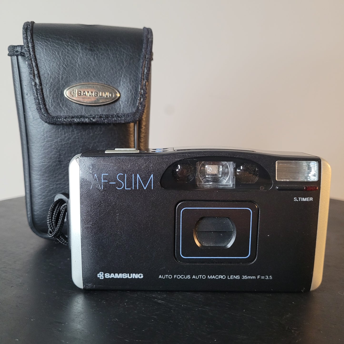 Samsung AF-Slim Kompaktkamera mit 35mm f/3.5 Makroobjektiv, Autofokus und eingebautem Blitz, zusammen mit einer schwarzen Black's Kameratasche.