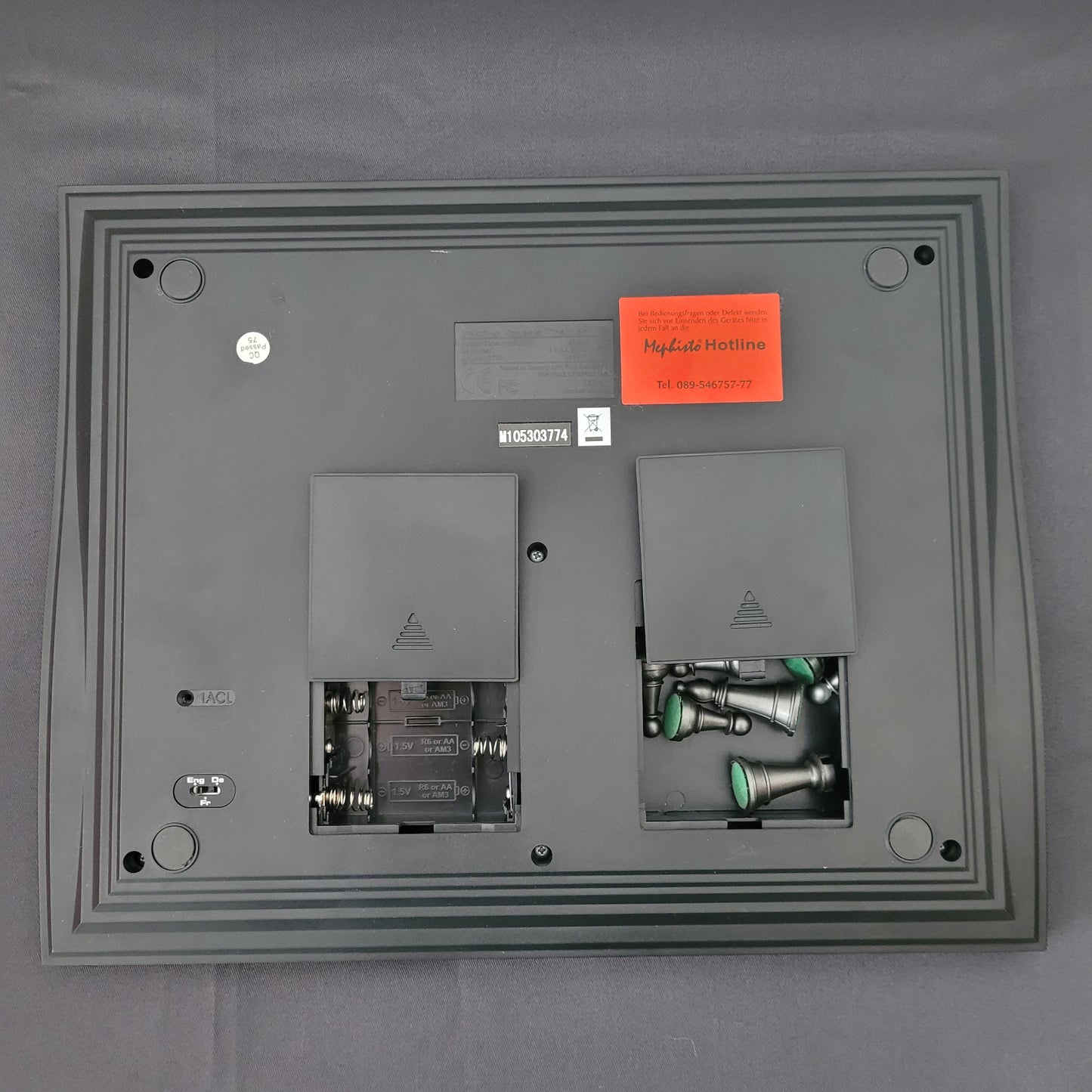 Das Bild zeigt die Rückseite des Schach Mephisto Talking Chess Trainer von Saitek. Sichtbar sind die integrierten Fächer zur Batterieaufnahme und zur Figurenaufbewahrung, die eine geordnete Unterbringung ermöglichen. Das Gerät liegt auf einem schwarzen Untergrund.