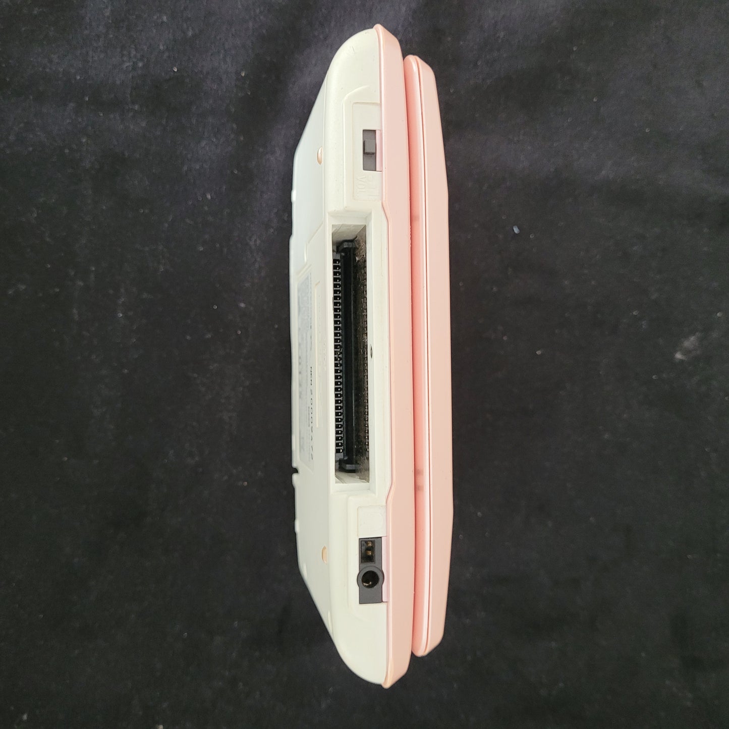Seitenansicht der Nintendo DS Pink Model No NTR-001 Handheld Konsole, liegend auf schwarzem Untergrund.