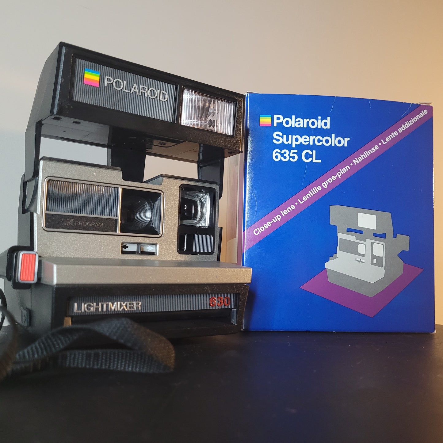 Polaroid Supercolor 635 CL Sofortbildkamera-Set auf einem Tisch, neben der Originalverpackung. Die Verpackung zeigt das Modell und hebt die Nahlinse hervor. Perfekt für Liebhaber von Vintage-Fotografie.