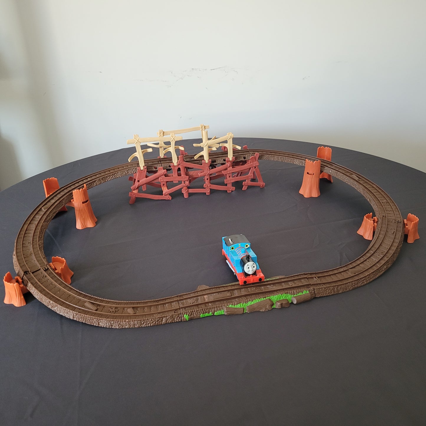 Das vollständige Thomas und seine Freunde Shake, Shake Bridge Playset, bestehend aus der Brücke, den dazugehörigen Schienen und der Lokomotive Thomas. Das Set ist auf einem schwarzen Untergrund arrangiert, während der Hintergrund weiß ist, wodurch die einzelnen Elemente besonders gut zur Geltung kommen.