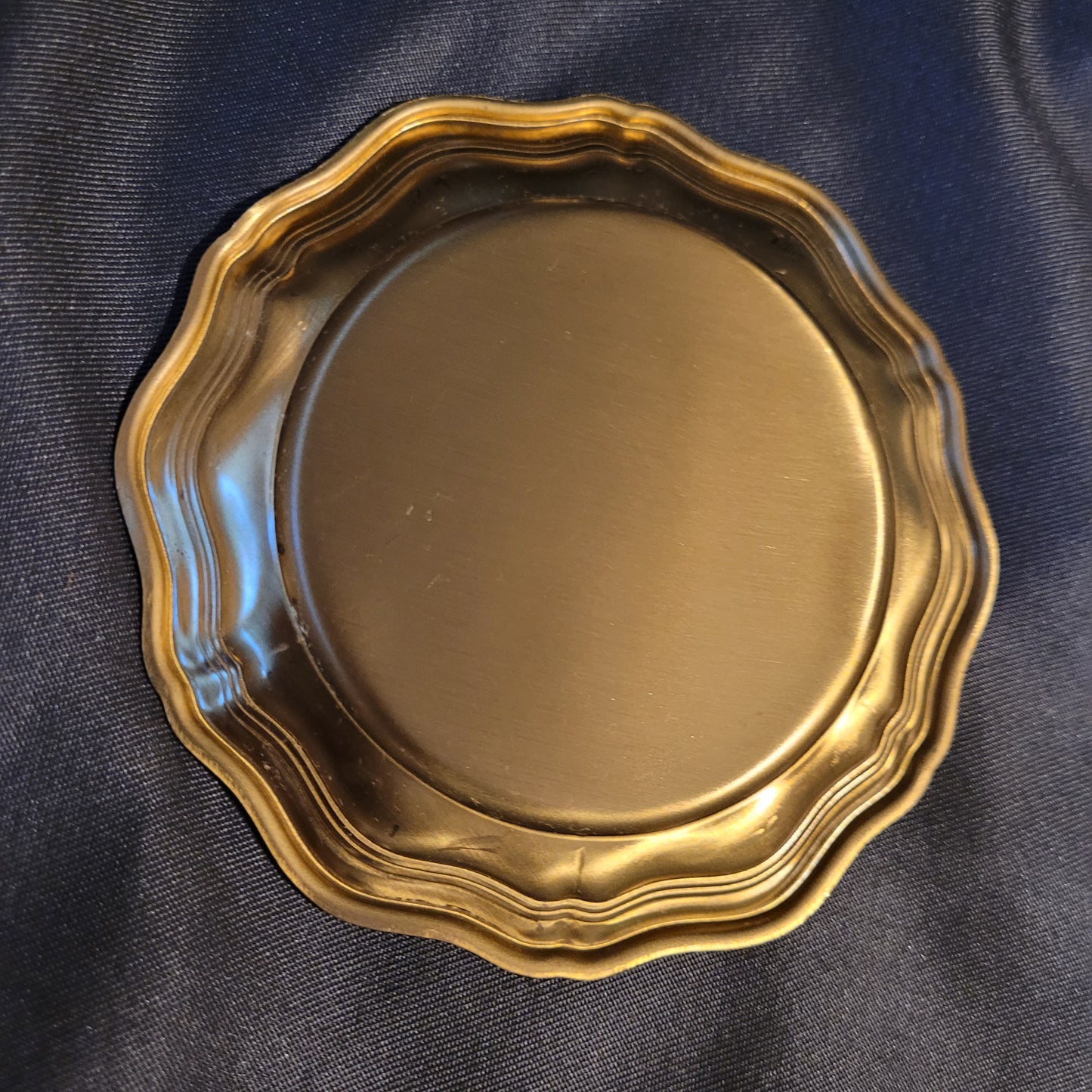 Untersetzer Mid Century Messing Vintage, einzelne Rückseite in leichter diagonaler Aufnahme, goldfarben, durch Licht silbern wirkend, schwarzer Hintergrund.