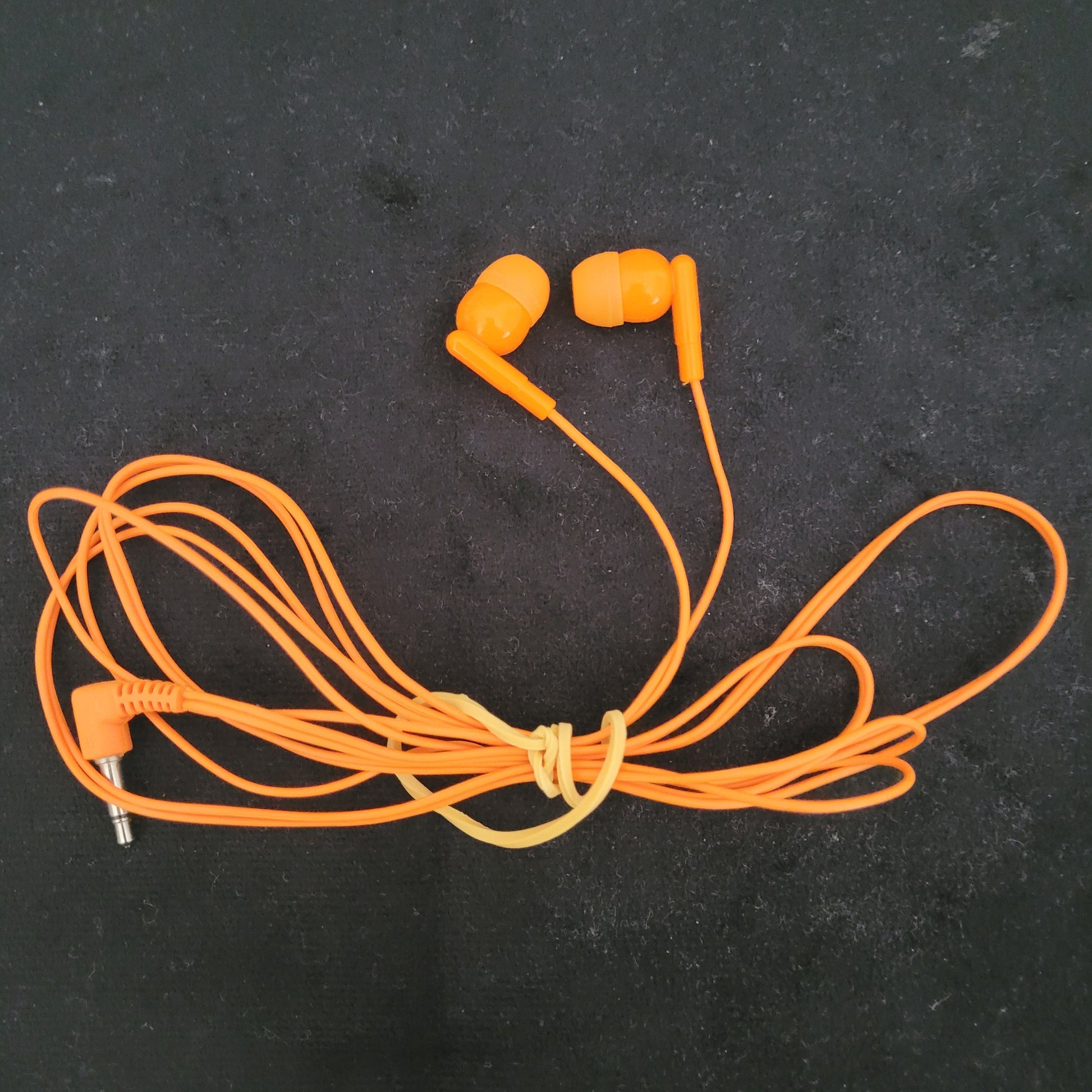 Orangefarbene In-Ear-Kopfhörer mit 3,5mm Klinkenstecker, zusammengebunden mit gelbem Gummiband – Vintage-Design auf dunkler Oberfläche, ideal für Musikliebhaber und Retro-Audiozubehör.