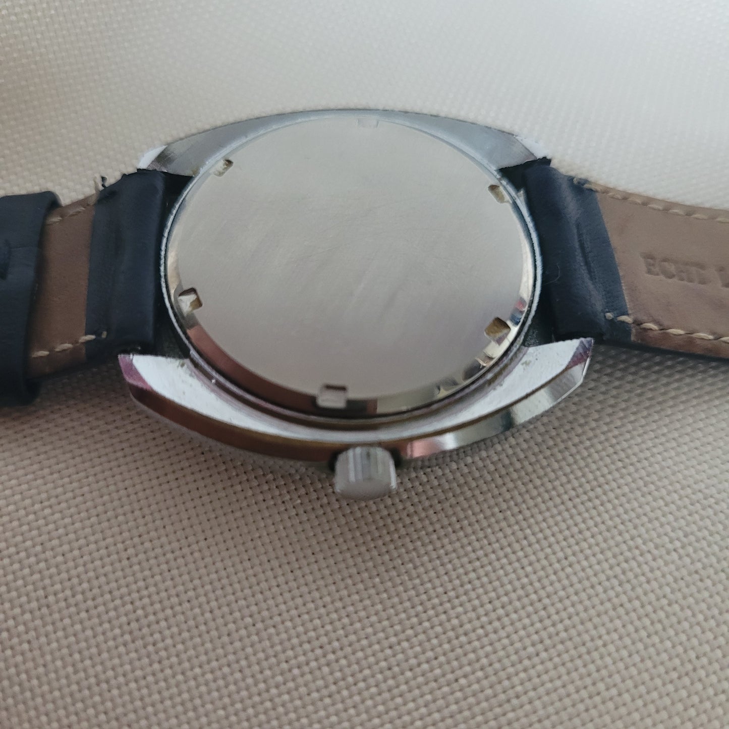 Alpina Vintage Armbanduhr Rückseite mit rundem Edelstahlgehäuse und schwarzem Lederarmband. Die glatte Gehäuserückseite zeigt altersgerechte Spuren, das Lederband ist außen schwarz und innen braun mit sichtbarer Naht – klassische Schweizer Vintage-Uhr für Sammler.