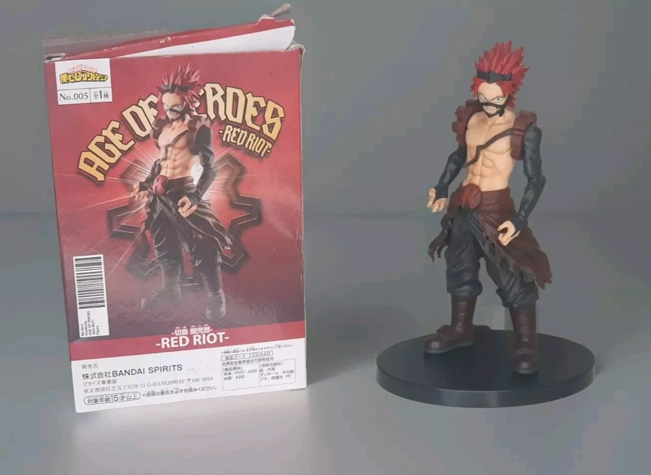Actionfigur "Red Riot" aus der Serie "Age of Heroes" neben der Verpackung auf schwarzem Sockel.