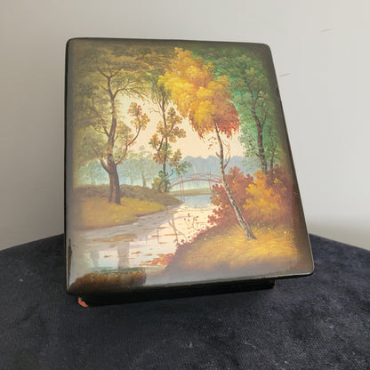 Antike/Vintage Lackdose aus Holz aus der UdSSR mit handbemaltem Landschaftsmotiv – Seltenes Sammlerstück mit Signatur Das Bild zeigt eine kunstvoll handbemalte Antike/Vintage Lackdose aus Holz aus der UdSSR. Die edle Lackdose ist mit einem detailreichen herbstlichen Landschaftsmotiv versehen, das bunte Bäume, eine Brücke und einen Fluss oder See im Hintergrund zeigt. Mit ihrer nostalgischen Gestaltung und der nicht eindeutig identifizierbaren Signatur ist sie ein seltenes Sammlerstück.