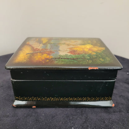 Antike/Vintage Lackdose aus Holz aus der UdSSR – Seitenansicht mit kunstvollem Landschaftsmotiv Das Bild zeigt die Seitenansicht einer antiken/Vintage Lackdose aus Holz aus der UdSSR, verziert mit einer handgemalten, detailreichen Herbstlandschaft. Farbige Bäume in warmen Gelb-, Orange- und Grüntönen prägen das Motiv, während im Hintergrund eine elegante Brücke über einen Fluss oder See zu sehen ist. Der Deckel der Lackdose ist leicht geöffnet.