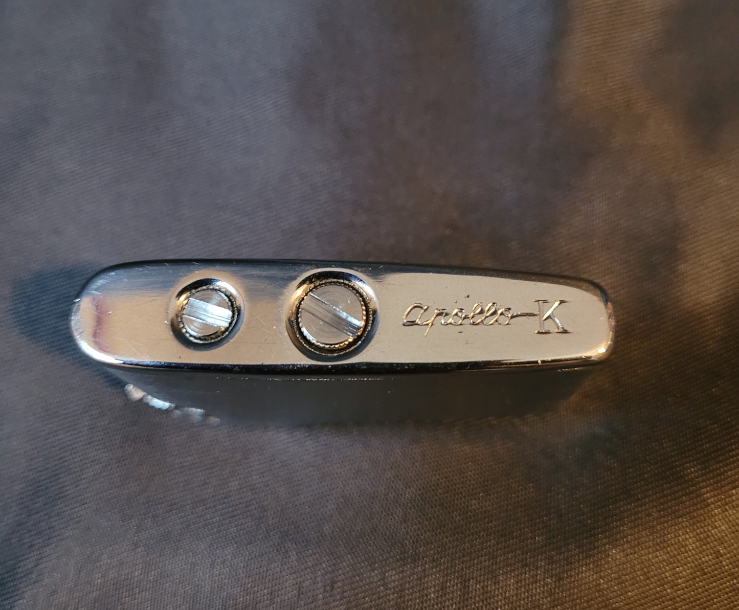 Apollo-K Feuerzeug Vintage, silberfarben, Unterseite mit Gasnachfüllöffnung, Hintergrund schwarz, kompaktes Sammler-Feuerzeug.