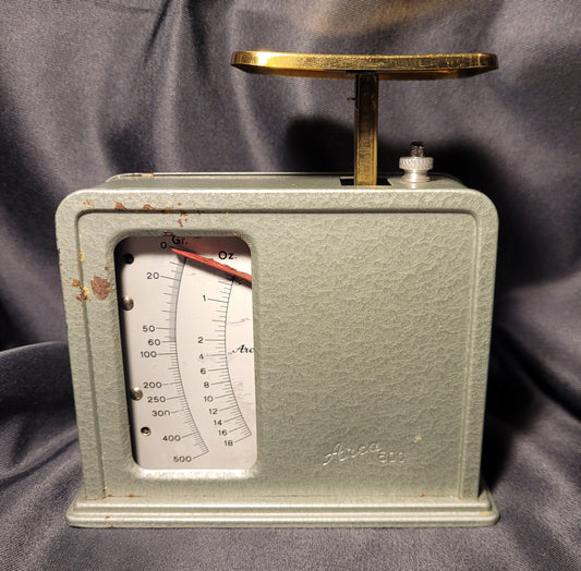 Arca 500 Briefwaage Küchenwaage Mid Century Vintage, Vorderansicht, leicht grünlich oder silbern schimmernd, schwarzer Hintergrund, kompaktes Design 14 × 13,5 × 6 cm. Eichfunktion sichtbar.