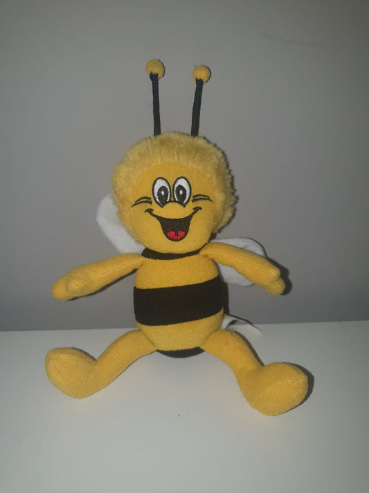 Biene Maja Stofftier mit schwarzen Streifen und großen, fröhlichen Augen sitzt auf einer weißen Oberfläche. Das Plüschtier hat zwei schwarze Fühler mit gelben Spitzen und weiße Flügel. Ideal für Kinder und Bienenliebhaber.