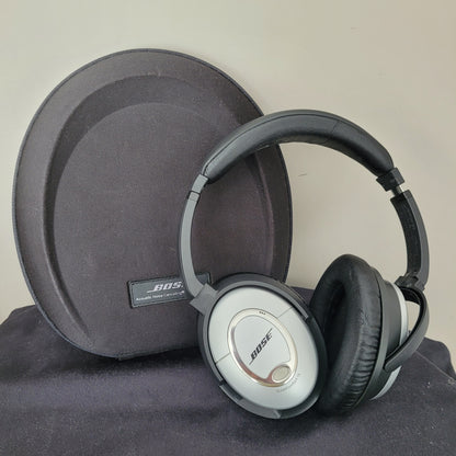 Die Bose Kopfhörer QuietComfort 15 liegen auf einer schwarzen, ovalen Tragetasche und präsentieren sich im klassischen Vintage-Design. Die silbernen Ohrmuscheln mit schwarzen Polstern unterstreichen den hochwertigen Look, während das Bose-Logo und die Modellbezeichnung „QuietComfort 15“ gut sichtbar sind. Die Tragetasche mit Bose-Branding vervollständigt das Set – ein Must-have für Liebhaber von Vintage-Elektronik und erstklassigen Kopfhörern.