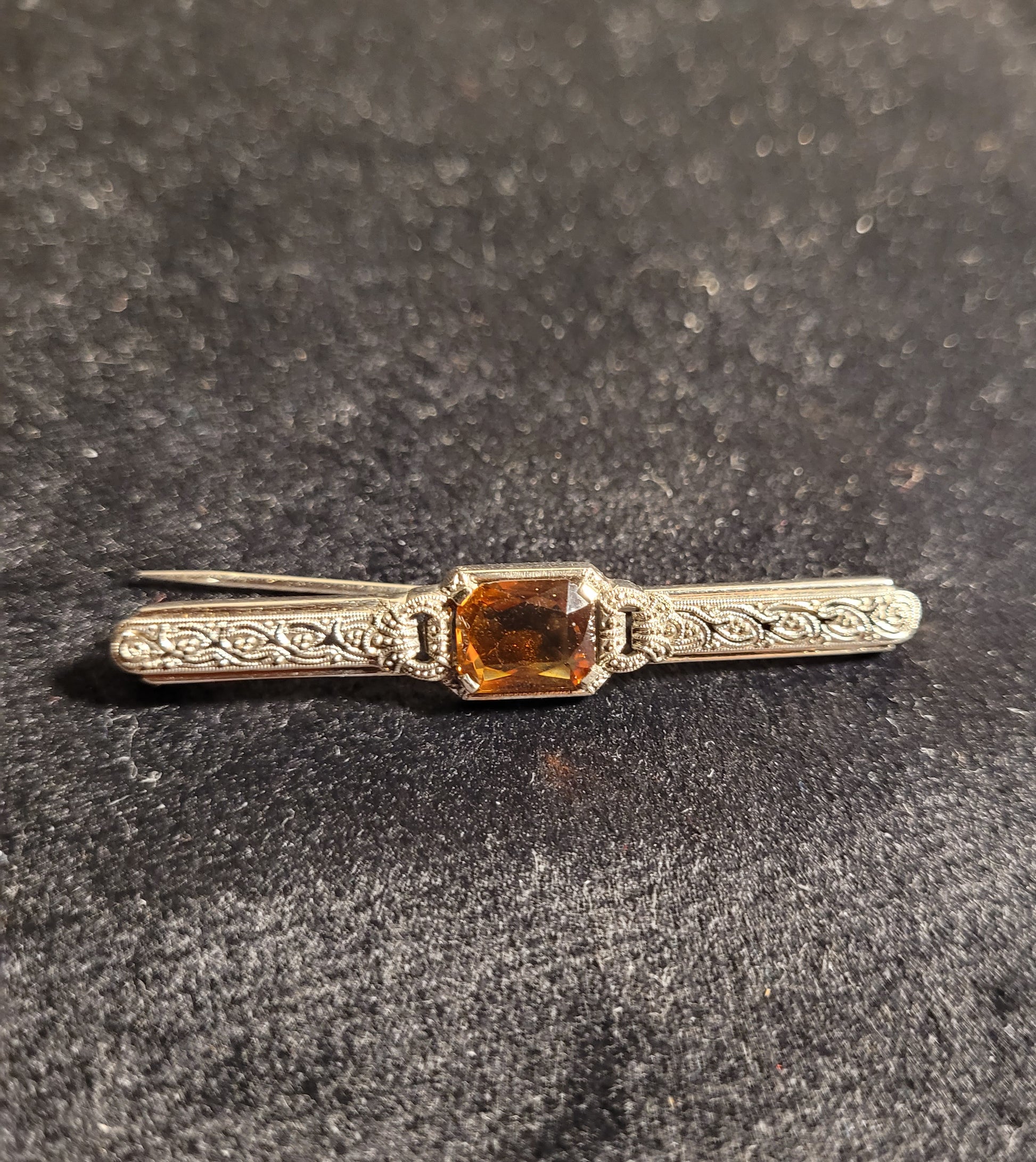 Antike silberne Brosche mit filigranen Verzierungen und rechteckigem, orangefarbenem Edelstein auf schwarzem Hintergrund.