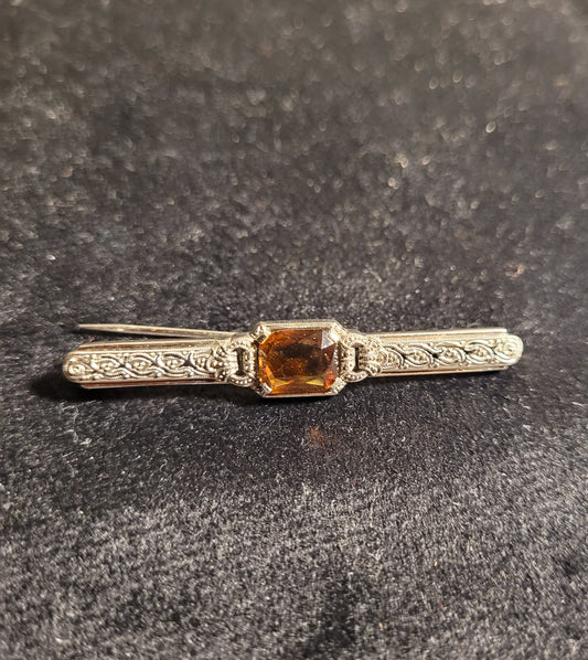 Antike silberne Brosche mit filigranen Verzierungen und rechteckigem, orangefarbenem Edelstein auf schwarzem Hintergrund.