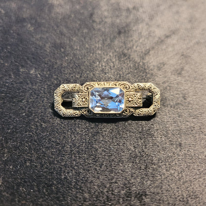 Vorderseite einer antiken Brosche mit rechteckigem, facettiertem blauem Edelstein und kunstvollem metallischen Design, verziert mit detaillierten Gravuren und Mustern
