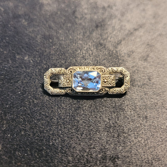 Vorderseite einer antiken Brosche mit rechteckigem, facettiertem blauem Edelstein und kunstvollem metallischen Design, verziert mit detaillierten Gravuren und Mustern