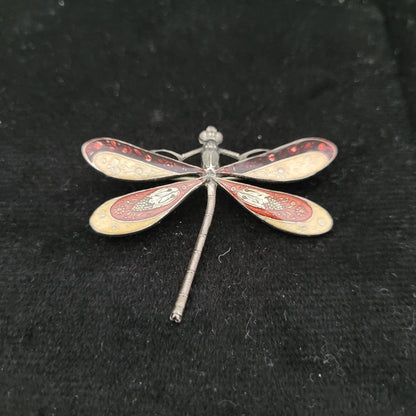 Detailaufnahme einer kunstvoll gestalteten Libellenbrosche. Die Brosche hat filigrane Flügel mit roten und goldenen Verzierungen und liegt auf schwarzem Hintergrund. Maße: 3,5x5 cm, nicht magnetisch.