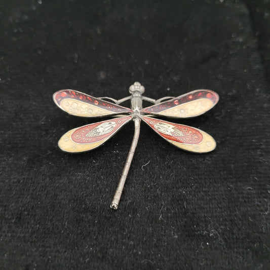 Detailaufnahme einer kunstvoll gestalteten Libellenbrosche. Die Brosche hat filigrane Flügel mit roten und goldenen Verzierungen und liegt auf schwarzem Hintergrund. Maße: 3,5x5 cm, nicht magnetisch.