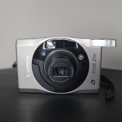 Canon IXUS Z70 Kamera in Nahaufnahme, silbernes Gehäuse mit eingebautem Blitz und Canon Zoomobjektiv 23-69mm, elegantes kompaktes Design.