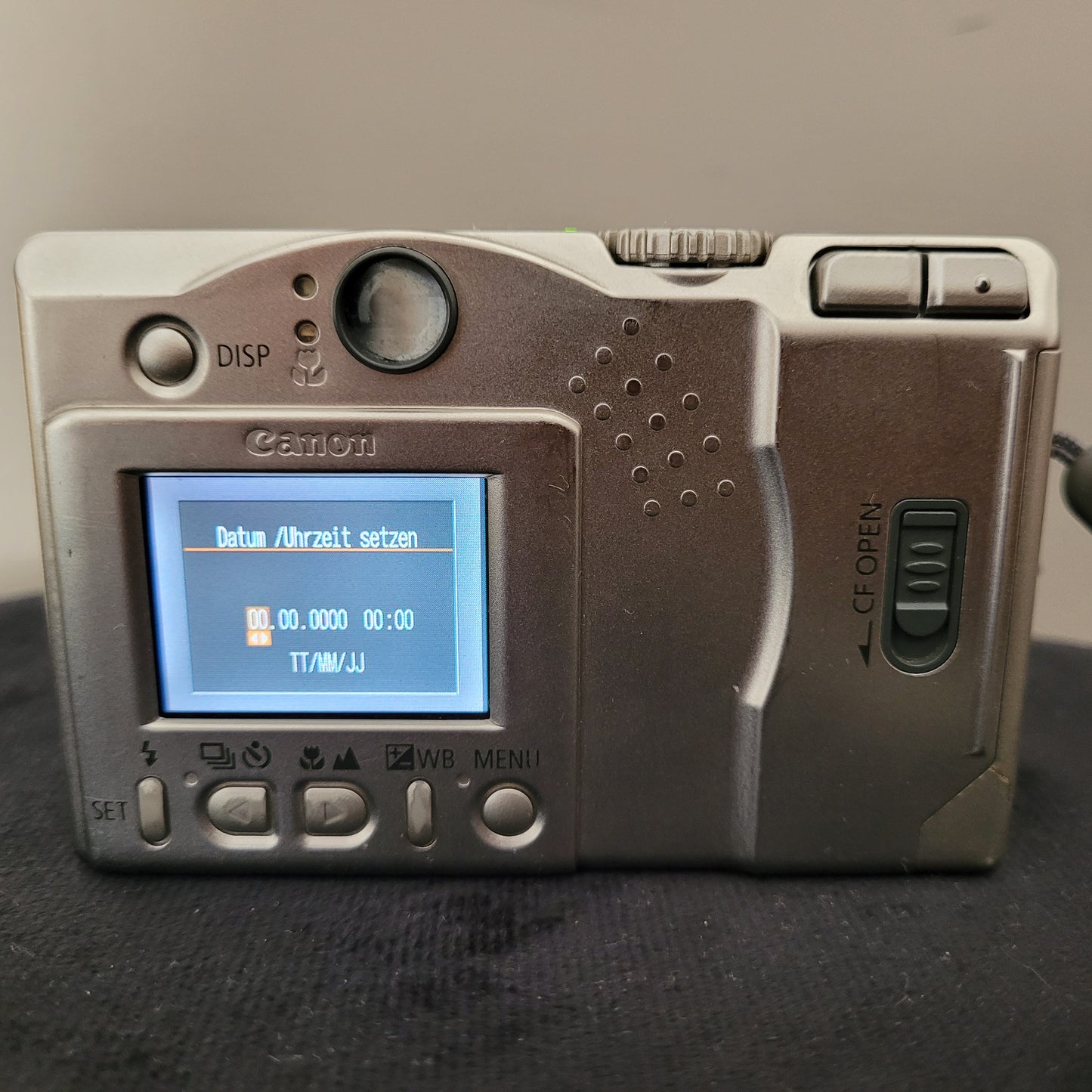 Rückseite einer Canon Digitalkamera mit Display. Menü zur Einstellung von Datum und Uhrzeit sichtbar. Mehrere Tasten und Bedienelemente, darunter \"DISP\" und \"MENU\" Tasten.