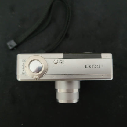Obenansicht der Canon Vintage Kamera Ixus II S mit ausgefahrenem Objektiv, sichtbarem Auslöser und Zoomhebel – klassische Kompaktkamera im Retro-Design für Sammler und Fans nostalgischer Canon-Technik.