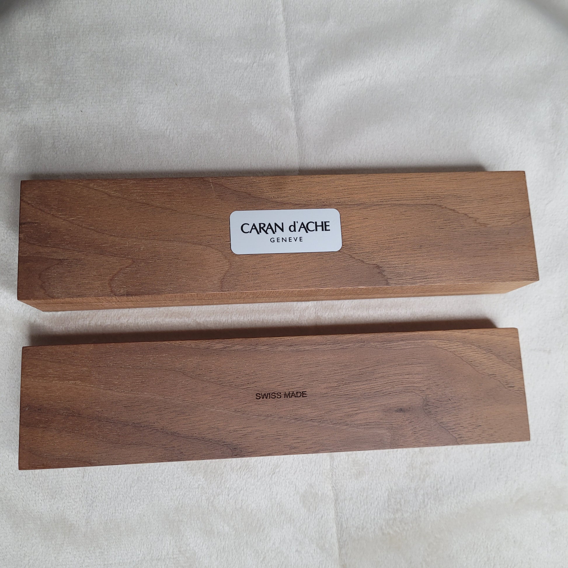 Set aus vier hochwertigen Caran d'Ache Bleistiften mit palladiumbeschichteten Kappen, präsentiert in einer eleganten hellbraunen Holzbox mit der Aufschrift 'CARAN D'ACHE GENEVE'.
