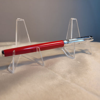 Caran d'Ache Kugelschreiber - Swiss Made, rotes Gehäuse, silberne Kappe, auf transparentem Ständer.
