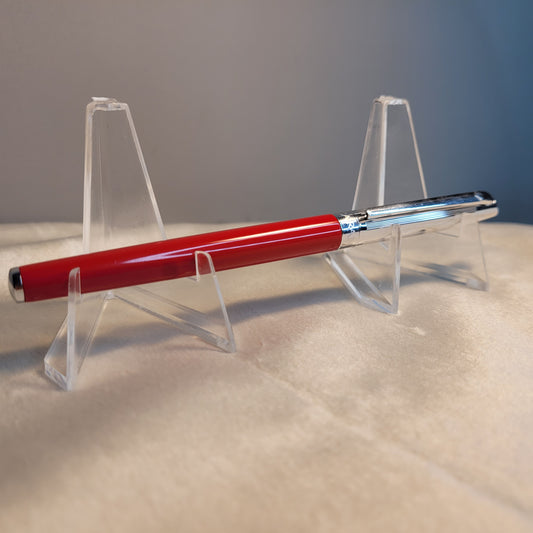 Caran d'Ache Kugelschreiber - Swiss Made, rotes Gehäuse, silberne Kappe, auf transparentem Ständer.