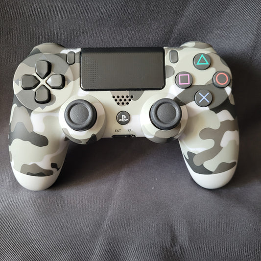 Original Sony Controller "Camouflage" – PlayStation 4 / PS4 – DualShock 4 in grau‑schwarz‑weißem Tarnmuster, mit Touchpad, Analog‑Sticks, Steuerkreuz und Aktionstasten, liegend auf dunkler Stoffoberfläche. EAN 0711719453512 / Modell CUH-ZCT1E.