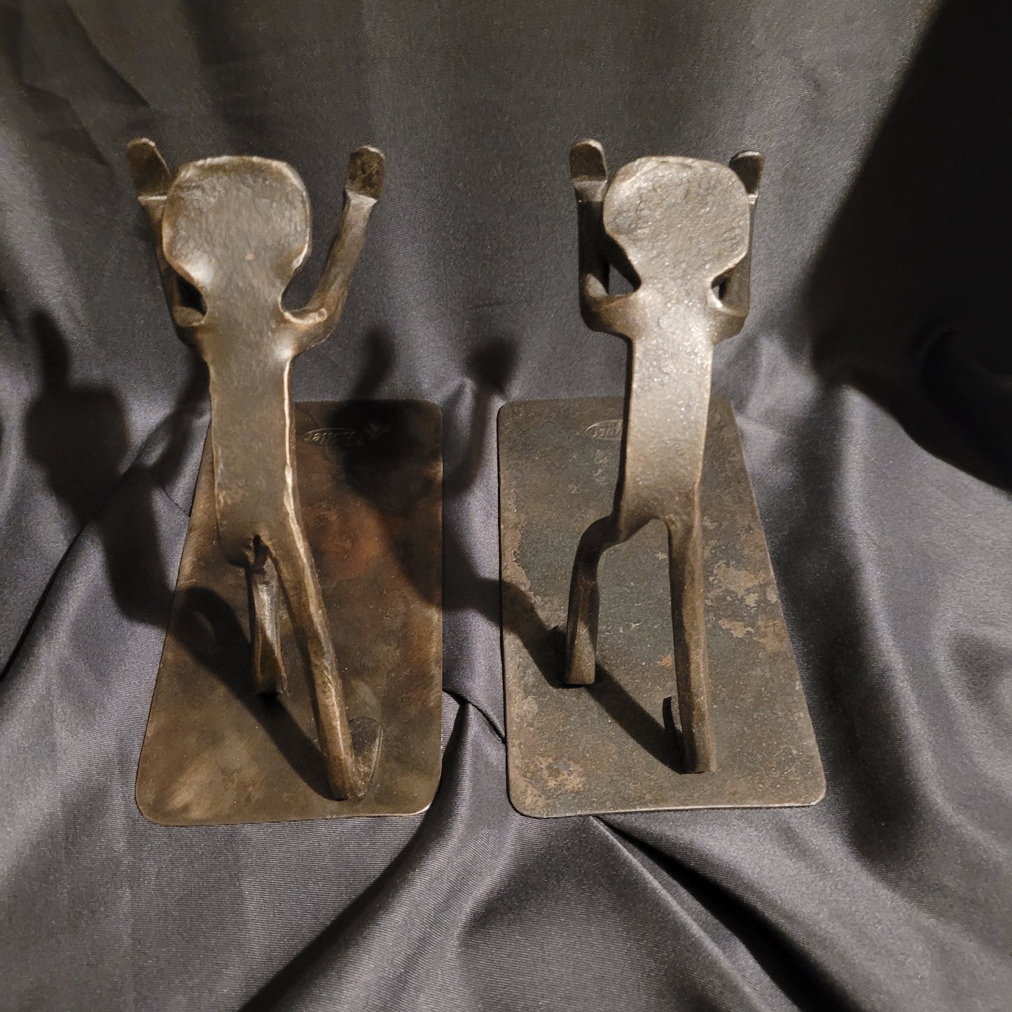 Draufsicht auf die massiven Metall-Buchstützen der Marke Höller. Gut zu erkennen ist die rohe, handgearbeitete Schmiedekunst und die stabile, breite Auflagefläche aus dunklem Eisen, die typisch für das modernistische Mid-Century Design ist.