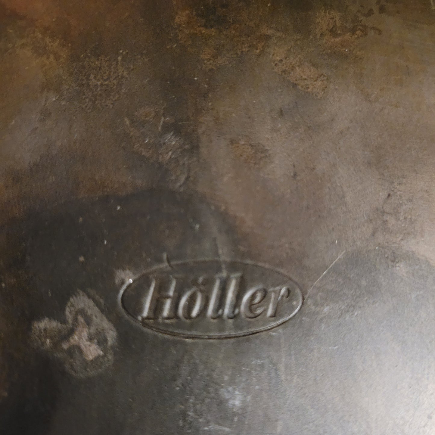 Nahaufnahme der authentischen Herstellersignatur 'Höller' in einer ovalen Prägung auf dem massiven Eisen. Dieses Qualitätsmerkmal bestätigt die Herkunft aus der renommierten deutschen Kunstschmiede für hochwertige Vintage-Objekte.