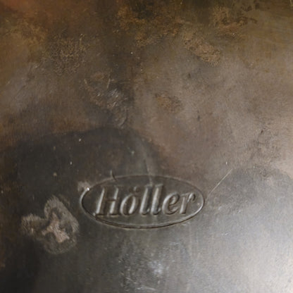 Nahaufnahme der authentischen Herstellersignatur 'Höller' in einer ovalen Prägung auf dem massiven Eisen. Dieses Qualitätsmerkmal bestätigt die Herkunft aus der renommierten deutschen Kunstschmiede für hochwertige Vintage-Objekte.