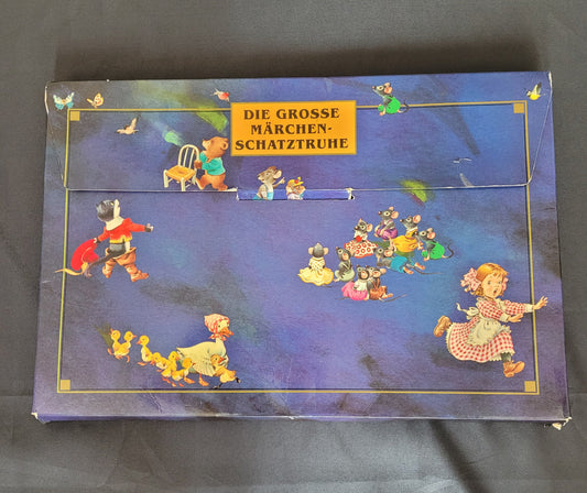 Vintage Kinderbuch-Set „Die große Märchenschatztruhe“ mit farbenfroher Illustrationen klassischer Märchenfiguren auf dunkelblauem Hintergrund. Die nostalgische Pappbox zeigt detailreiche Szenen mit Tieren in Kleidung, märchenhaften Charakteren und liebevoll gestalteten Motiven – ideal für Sammler und Liebhaber von Vintage-Märchenbüchern.